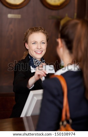Smiling Stylish Young Receptionist Handing Out A Business Card To A Customer In A Hotel Lobby