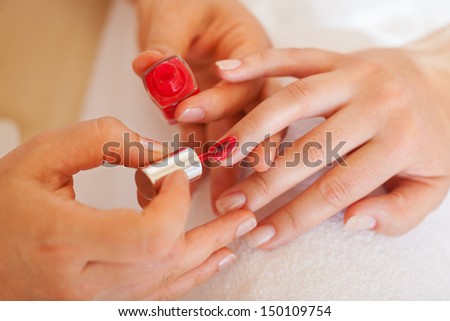 Woman enjoying a manicure in a beauty salon having red nail varnish applied to her nails by a beautician, cropped view of the hands