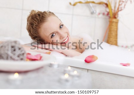 Beautiful woman relaxing in a foamy bubble bath resting her head on the side and smiling at the camera in appreciation and enjoyment