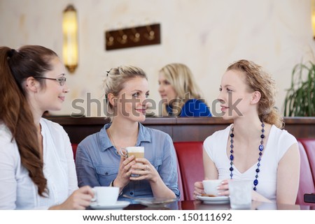 Three attractive stylish young female friends drinking coffee together and chatting in a cafe