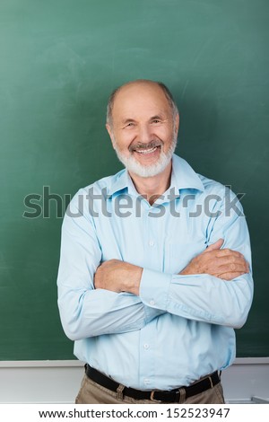 Vertical portrait of Confident expert teacher looking at camera while sitting with arms folded with a blank chalkboard behind