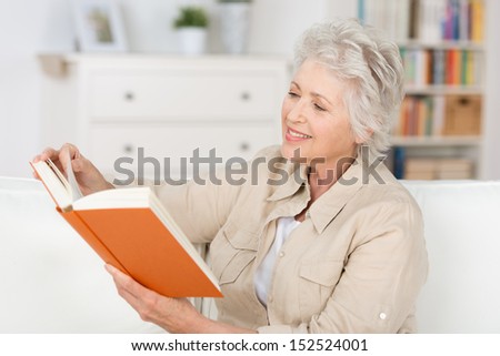 Attractive stylish elderly woman relaxing at home reading a book in her living room