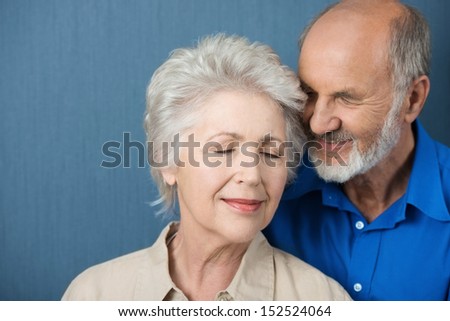 Elderly couple share a tender moment of love as they stand close together with their eyes closed in contentment and bliss
