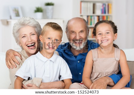 Happy Young Boy And Girl With Their Laughing Grandparents Smiling At The Camera As They Pose Together Indoors