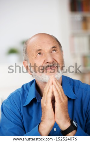 Worried religious senior man praying to god with his hands raised and touching as he looks beseechingly towards heaven for help and inspiration