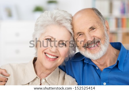 Affectionate happy retired couple with their heads together in a close embrace smiling at the camera