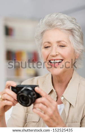 Vertical portrait of a happy caucasian senior woman setting her compact camera
