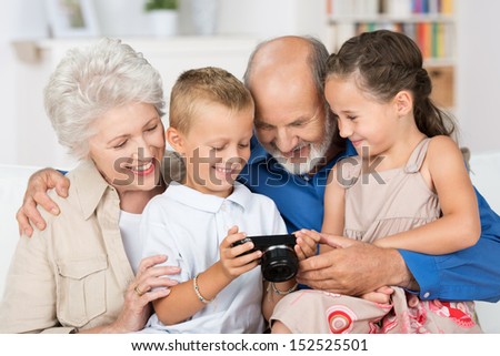 Two beautiful happy young grandchildren with their grandparents in a close group looking at the back of a camera at a photograph