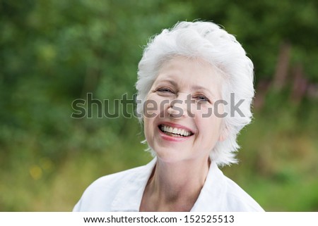 Vivacious laughing grey haired senior woman outdoors in a lush green park, close up portrait