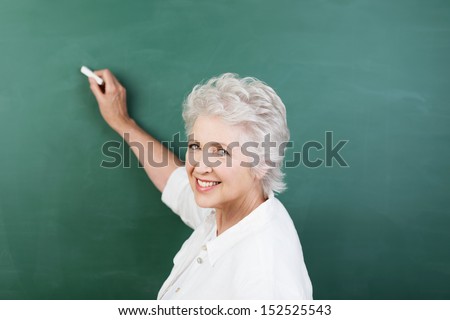 Senior woman writing on a blank chalkboard during a college class or business presentation turning to look back and smile at the camera