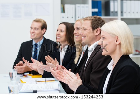 Smiling business people clapping their hands at the end of a meeting or presentation or in recognition of an achievement by one of their colleagues