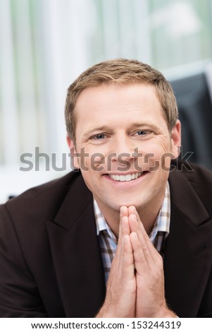 Smiling handsome young businessman with a friendly smile sitting with his hands clasped in front of him as though praying