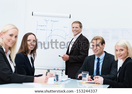 Successful business design team with diverse young men and women seated at a conference table discussing a presentation diagram on a flipchart