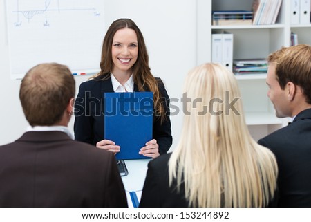 Young attractive female applicant sitting at a table holding a file at a job interview facing a row of corporate business executives who are conducting the interview