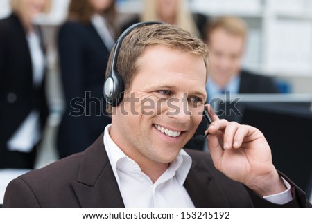 Handsome Young Businessman With A Warm Smile Taking A Call On A Headset As He Deals With Queries At The Customer Support Call Centre