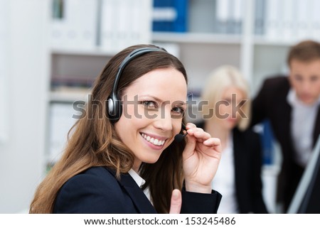 Happy attractive young female call centre operator or receptionist wearing a headset turning to give the camera a friendly smile