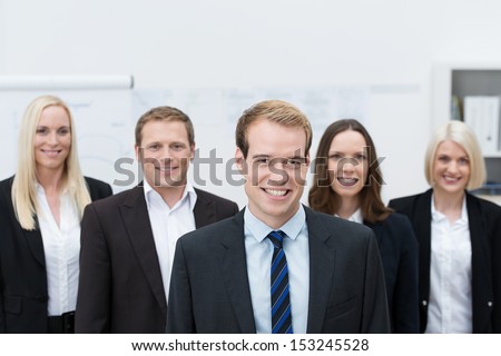 Handsome young Caucasian manager smiling with a happy team made of three women and a man, behind him