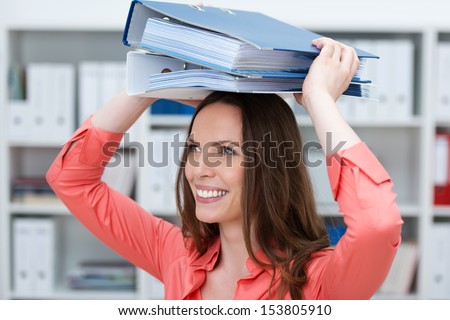 Playful young female business clerk with folders balanced on her head smiling happily