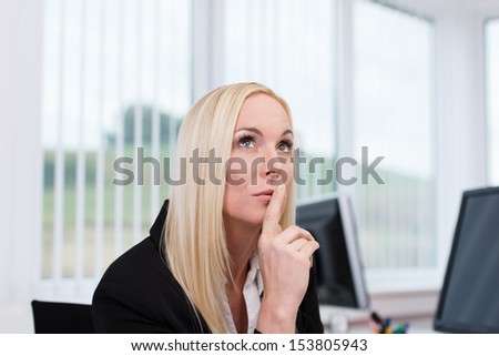 Thoughtful businesswoman making decisions sitting at her desk looking up into the air with her finger to her lips