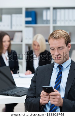 Businessman reading a text message on his mobile phone while sitting in a busy corporate office