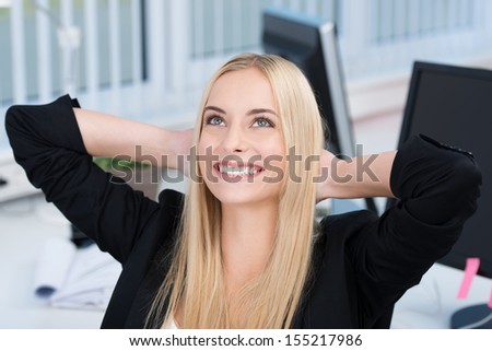 Beautiful businesswoman daydreaming leaning back in her chair with her hands behind her head looking up with a beaming smile