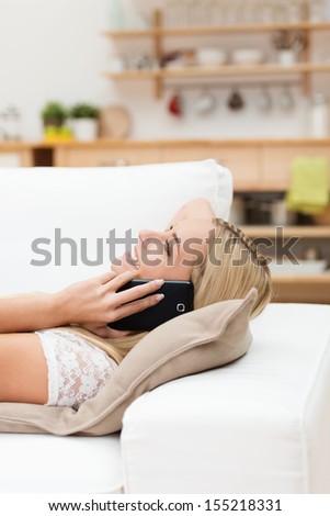 Woman having an enjoyable conversation on her mobile while lying relaxing on a sofa in her living room