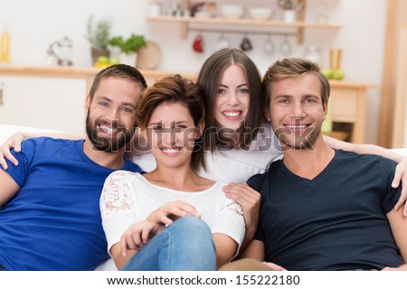 Group of happy young men and women grouped close together on a sofa in their home smiling at the camera