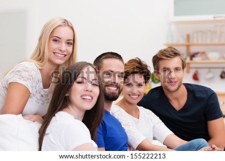 Group Of Young Men And Women Relaxing At Home On A Living Room Sofa Turning To Smile At The Camera With Focus To A Bearded Young Man In The Centre