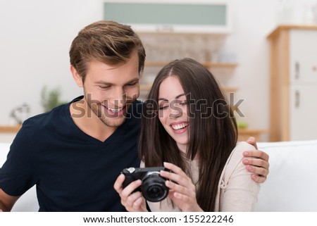 Happy affectionate young couple checking a photo on the back of their camera as they sit close together on a sofa in the living room