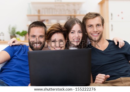 Smiling group of young men and women sitting in a row on a sofa sharing a laptop computer