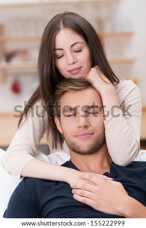Romantic young couple sharing a loving moment in their living room sitting in an intimate embrace with their eyes closed in bliss