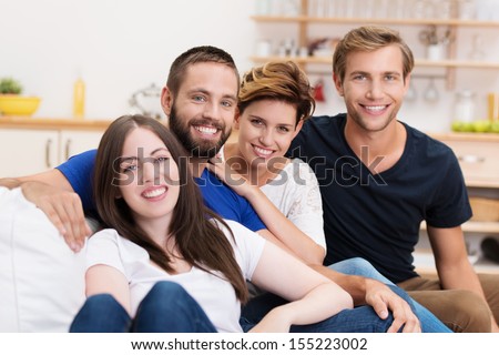 Group of diverse young friends relaxing at home grouped together on a sofa and smiling happily at the camera