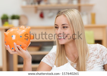 Happy young woman relaxing at home looking at her piggy bank with a lovely beaming smile as she contemplates her nest egg, goals and dreams