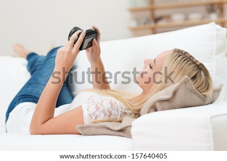 Blond woman lying on her back on a sofa checking her images on the back of a digital camera