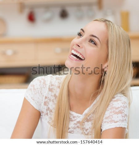Laughing Happy Young Blond Woman Sitting On A Couch In The Living Room Looking Up With A Joyful Smile