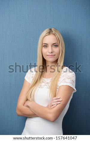 Confident friendly young blond woman standing with folded arms against a green background smiling at the camera