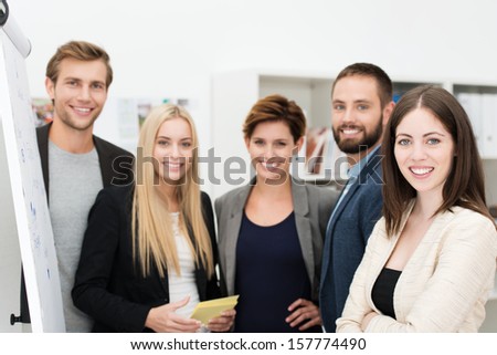 Smiling confident group of business people standing together in front of a flip chart having a discussion and sharing ideas