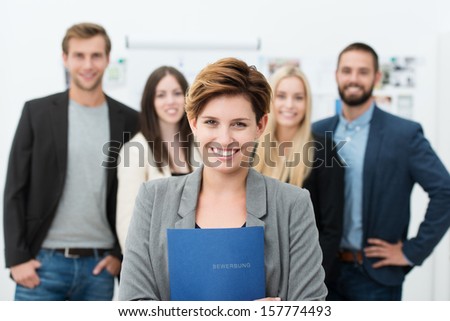 Group of job applicants with a smiling confident young woman in the foreground holding her Curriculum vitae in her hands