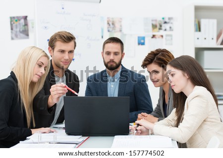 Serious Group Of Diverse Professional Young Business People In A Meeting Sitting At A Table Consulting Information On A Laptop Computer