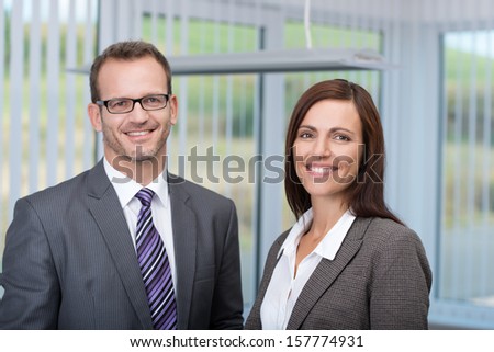 Smiling business partners with a successful confident man and woman posing side by side in the office smiling at the camera