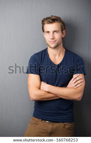 Self-assured handsome man standing with his arms crossed in smart casual clothing against a dark studio background