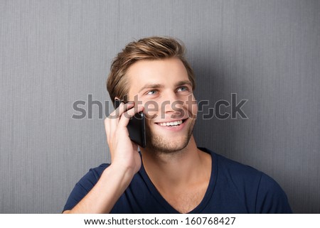 Young man chatting on a smartphone smiling with pleasure as he listens to the conversation, against a green studio background