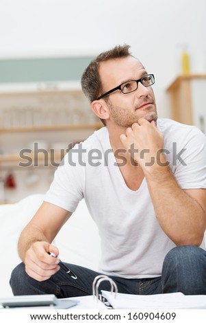 Handsome Young Man In Glasses Sitting On A Sofa In The Living Room Thinking And Staring Up Into The Air As He Works On Paperwork At Home