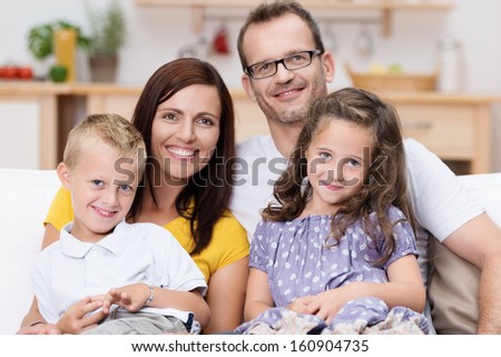 Happy Family With A Small Son And Daughter Sitting In A Group On The Sofa In The Living Room Smiling Happily At The Camera