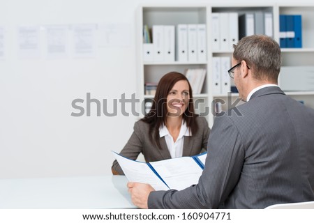 Businessman Conducting An Employment Interview With An Attractive Young Female Applicant Sitting Opposite Him At The Desk In The Office Answering His Question Concerning Her Cv