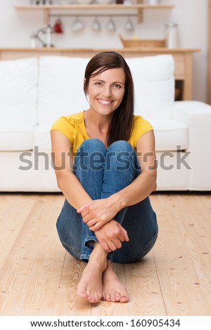 Happy adult woman sitting on her house floor with arms around her knees