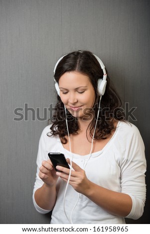 Beautiful young woman enjoying her music listening to tunes on her MP3 storage device on a headphones with a smile of pleasure and contentment