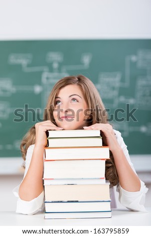 Young attractive smiling teenage girl dreaming in the classroom with her head resting on a tall stack of textbooks