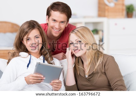 Young students, two attractive young women and a handsome young man, enjoying downloaded music on a tablet computer as they relax at home