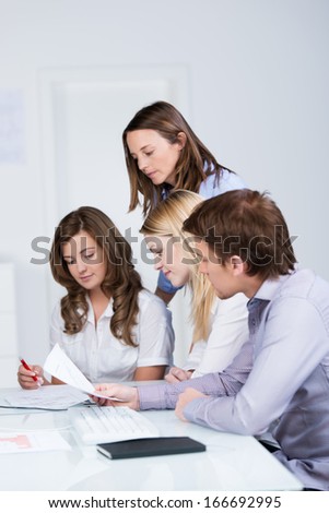 Group of young business people sitting together in a meeting grouped together reading a document held by one of the ladies